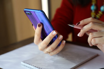 Fototapeta premium Girl makes notes in a notebook, uses a mobile phone wirelessly