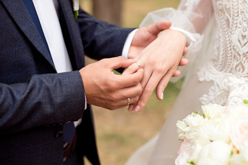 Groom wears bride a wedding ring Bride hand holds a beautiful wedding bouquet