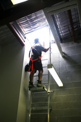 Construction worker wearing fall body harness standing resting on safe industrial ladder middle ...
