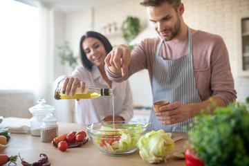Husband and wife seasoning salad while cooking lunch