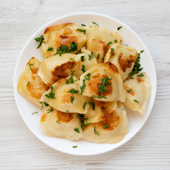 Homemade traditional polish fried potato pierogis on a white plate on a white wooden surface, top...