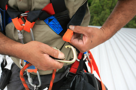 Close up pic of male industrial rope access worker wearing fall arrest, fall restraint safety protection harness clipping Carabiner into side safety harness loop prior work, construction building site
