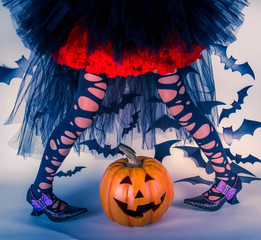 Halloween kids: little girl in witches shoes stands over smiley Halloween pumpkin with crooked legs