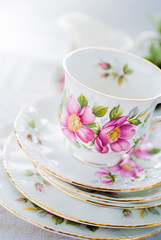 Vintage tea or coffee cup with gold rim on a stack of saucers. White linen tablecloth.