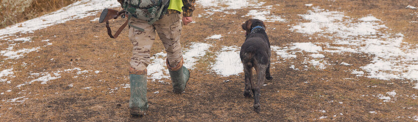 Hunting period, autumn season open. A hunter with a gun in his hands in hunting clothes in the autumn forest in search of a trophy. A man stands with weapons and hunting dogs tracking down the game.	