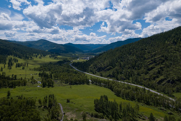 Fototapeta na wymiar Aerial landscape with mountains, green trees, field, road and river under blue sky and clouds in summer