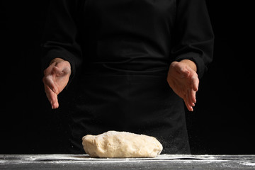 The cook works, makes the dough, kneads it in his hands on a black background. Freezing in motion. Cooking baking, culinary background, recipe book, menu