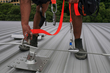 Male hand using transfer, clipping stainless industrial locking hook into the fall arrest roof...