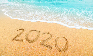 Happy New Year 2020, lettering on the beach with wave and  blue sea. Numbers 2020 year on the sea shore, New Years concept.