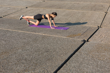 A young slim athletic girl in sportswear with snakeskin prints performs a set of exercises. Fitness and healthy lifestyle.	