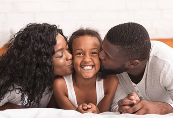 Loving black parents kissing cheeks of their happy little daughter
