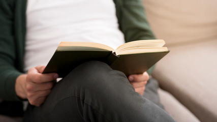 Cropped photo of man holding book, sitting on sofa
