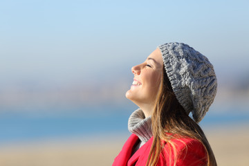 Happy woman breathing deeply fresh air on the beach in winter