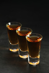 Three shots with whiskey at dark background