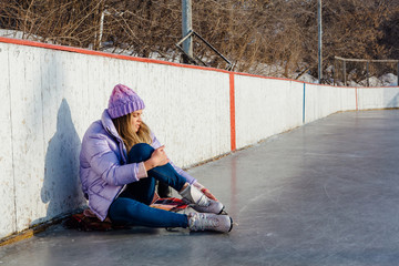Lovely young woman sitting on ice ring and tieing shoelaces