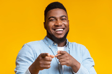 Joyful black guy pointing fingers at camera on yellow background
