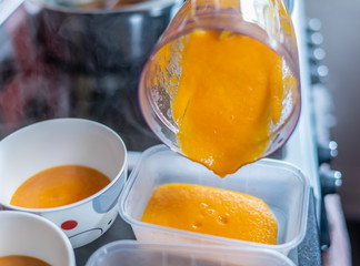 Close up of a jug of steaming hot homecooked carrot and ginger soup being portioned up in to containers