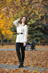 A young pretty brunette girl in a knitted sweater stands on a background of yellow trees while...