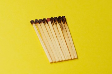Symbol of danger with matches on yellow  background top view , pile of burnt matches  arrange in a row with one  unBurnt match in the middle  , unlit matches , unique and various concept   