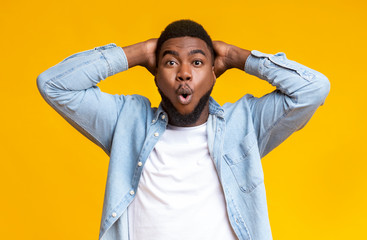 Amazed black guy holding hands behind head on yellow background