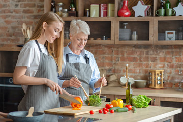 Young woman cooking healthy veggies salad with aged mom