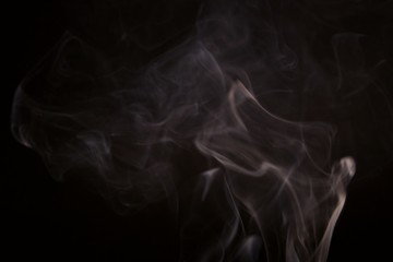 Fototapeta premium White steam spins and rises from the pan. White smoke rises from a large pot, which is located behind the frame. black background. Texture of smoky cloud