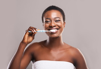 Portrait of beautiful african woman brushing teeth on gray background