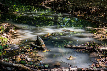 Small forest stream with muddy white water, sun glare on the water