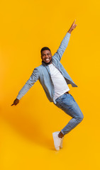 Cheerful African Man Standing On Tiptoes, Fooling Over Yellow Background