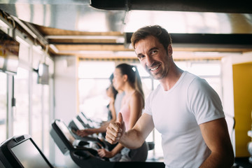 Fototapeta na wymiar Happy fit people running on treadmill at fitness gym club