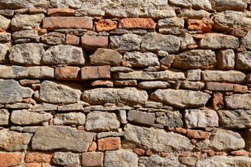 Texture of an old wall of stones and bricks lit by sunlight