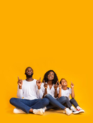 Afro family of three sitting on floor and pointing upwards