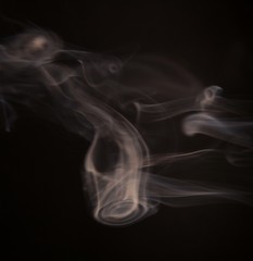 White steam spins and rises from the pan. White smoke rises from a large pot, which is located behind the frame. black background. Texture of smoky cloud