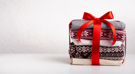 Stack of sweaters wrapped by red ribbon with bow on white