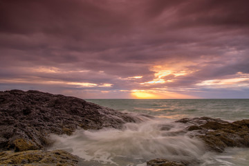 Dramatic sunset of seascape with strong wave hits rock on shore