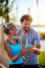 Modern woman and man jogging / exercising in urban surroundings and using cellphone at a pause / break.