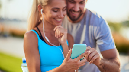 Modern woman and man jogging / exercising in urban surroundings and using cellphone at a pause / break.