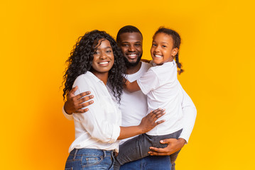 Young black parents with cute little daughter over yellow background