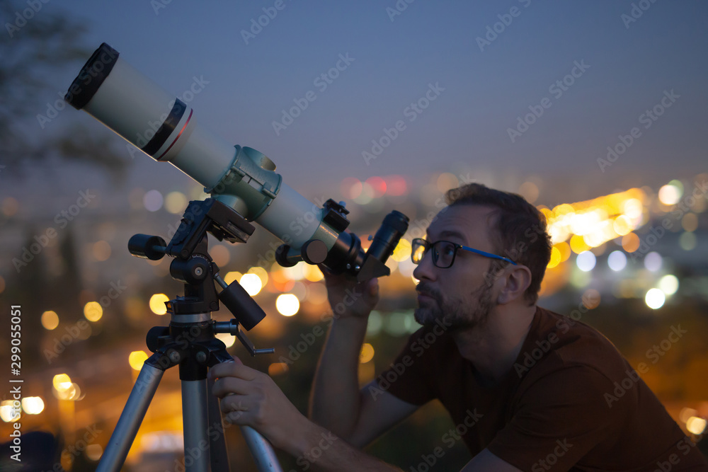 Wall mural astronomer with a telescope watching at the stars and moon with blurred city lights in the backgroun