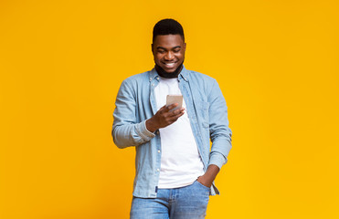 Cheerful black guy reading message on smartphone over yellow background