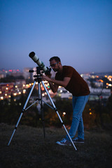 Astronomer with a telescope watching at the stars and Moon with blurred city lights in the...