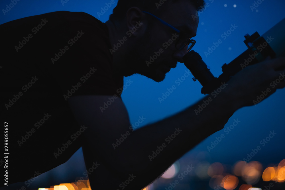 Wall mural astronomer with a telescope watching at the stars and moon with blurred city lights in the backgroun