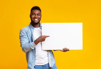 Handsome black guy holding and pointing at white advertising board