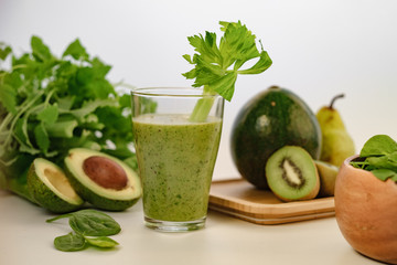 Green smoothie with a stalk of celery in a glass cup. On the table is an avocado.