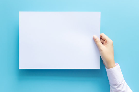 Close Up Hands Holding Empty White Blank Letter Paper Size A4 For Flyer Or Invitation Mock Up Isolated On A Blue Background.