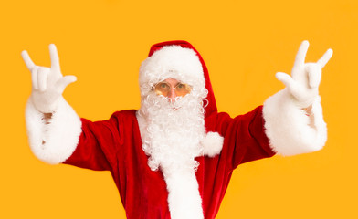 Young Santa in sun glasses showing horn sign on orange