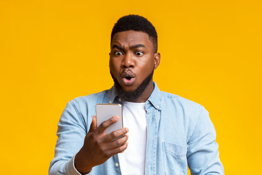 Astonished black guy looking at smartphone screen in shock