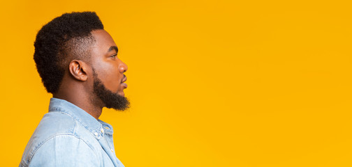 Profile portrait of serious bearded black guy on yellow background
