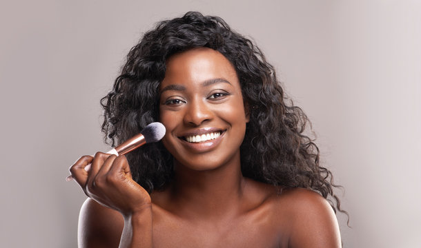 Beautiful african woman applying blush on face with brush tool