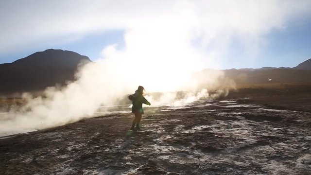 Silhouette of a dancing woman in front of steamy geyser in rocky mountain range at sunrise